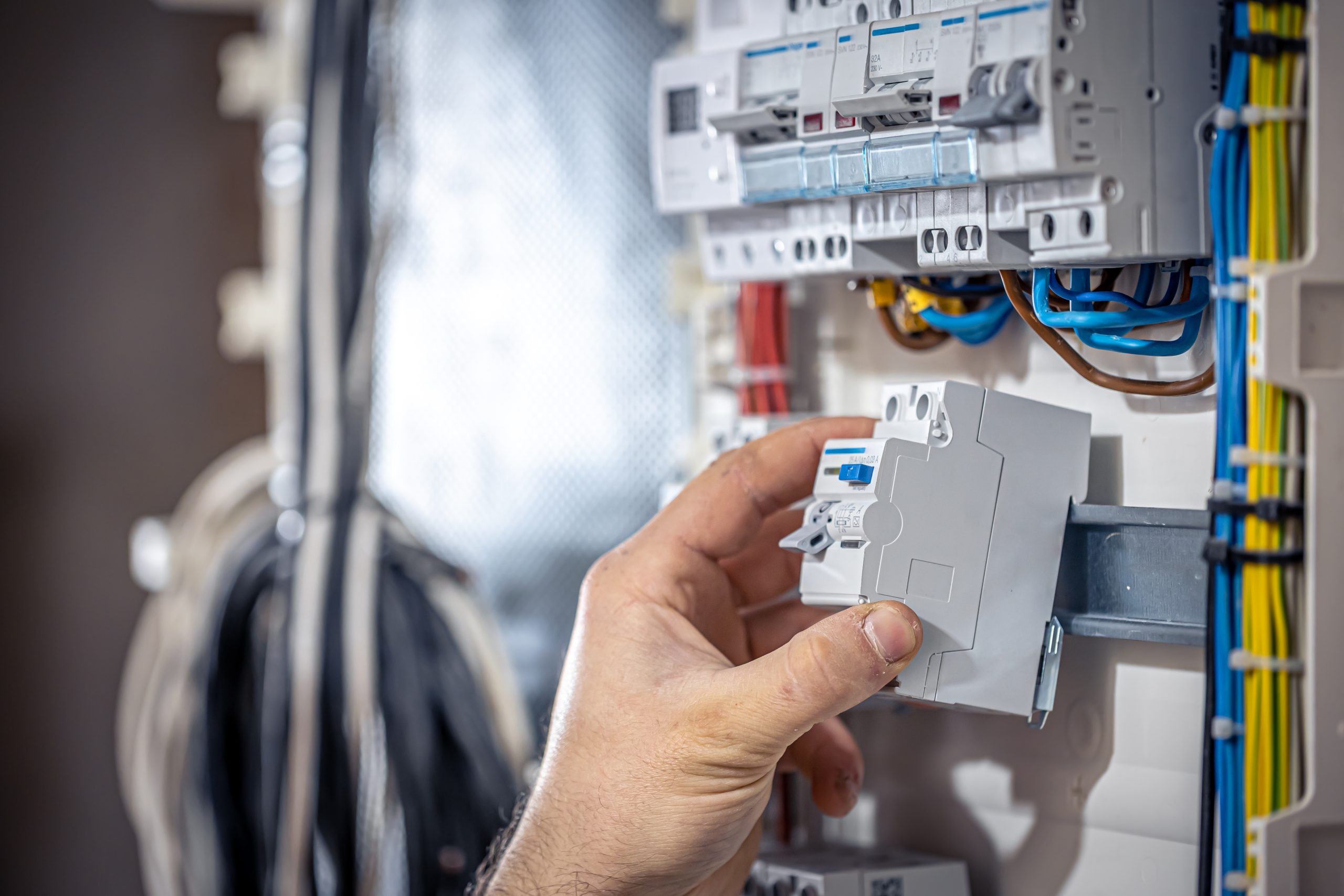 A male electrician works in a switchboard with an electrical connecting cable. Male electrician at the checkout counter on a blurred background of a switchboard.